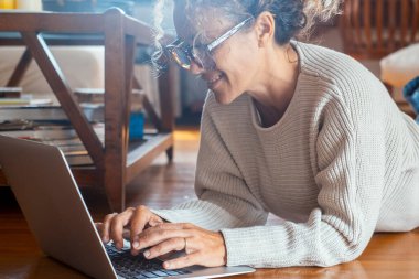  Evde dinlenen bir kadın dizüstü bilgisayarda evde yalınayak yere uzanmış yazıyor. Alternatif uzaktan çalışan ve zeki çalışan kadın yetişkin yaşam tarzı. Web Ara