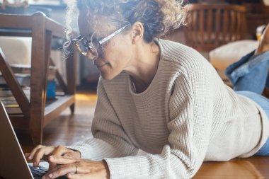 Alternatif ofis işyerinde dizüstü bilgisayarda çalışan modern bir bayan gündelik kıyafetlerle yerde yatıyor. Yetişkin kadınlar gözlük takıyor ve e-posta yazmak ya da internette arama yapmak için bilgisayar kullanıyorlar.