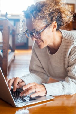  Evde dinlenen bir kadın dizüstü bilgisayarda evde yalınayak yere uzanmış yazıyor. Alternatif uzaktan çalışan ve zeki çalışan kadın yetişkin yaşam tarzı. Web Ara