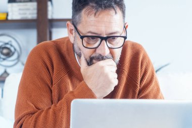 Kanepede dizüstü bilgisayara bakarak evde çalışan endişeli bir adam. Çevrimiçi güvenlik sorunları şifre kavramını kaybetti. Modern olgun erkek insanlar bilgisayarda koltukta oturuyor. Uzaktan kumandalı. Sörf ağı sosyal