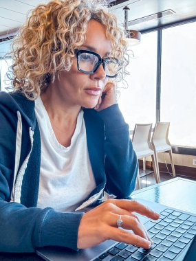 Gemi gezisi sırasında masada oturan güzel sarışın yönetici. Kıvırcık saçlı ve siyah gözlüklü bir kadın seyahat ederken laptop kullanıyor. Dijital göçebeler kavramı.