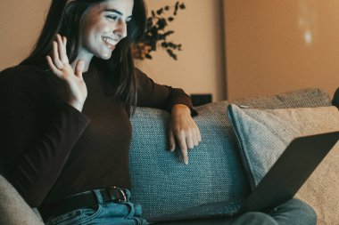 Mutlu esmer kız dizüstü bilgisayarla el sallıyor sanal sohbet videosunun tadını çıkarıyor uzaktan sanal görüşmede, rahatlamış ve arkadaşlarıyla konuşuyor..