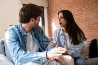 Üzgün suratlı bir kadın, kötü ilişki tartışmalarında koltukta oturan kıskanç bir adamdan özür diliyor. Sorunlar ve aldatmalar hakkında. Boşanma kavramını bozmak. Evde birlikte tartışıyoruz.