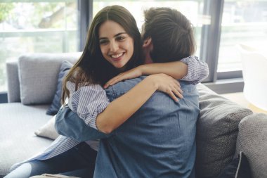 Kanepede oturmuş birbirlerine mutlu bir şekilde sarılan gülümseyen çift. Aşk ve mutluluk kavramı