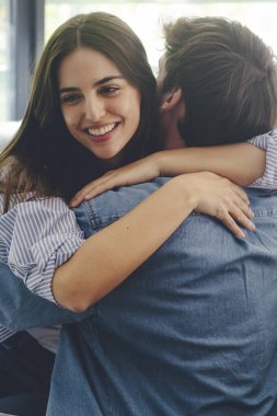 Kanepede oturmuş birbirlerine mutlu bir şekilde sarılan gülümseyen çift. Aşk ve mutluluk kavramı. Genç ve neşeli bir kadın en iyi arkadaşına ya da erkek arkadaşına sarılıyor. Kucaklayan kardeş arkadaş
