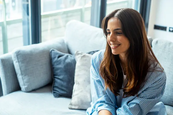 stock image Female psychological therapy session with woman sitting indoors on sofa smiling cheerfully. One adult young female thinking on the couch at home in daydreaming moment. Smiling happy