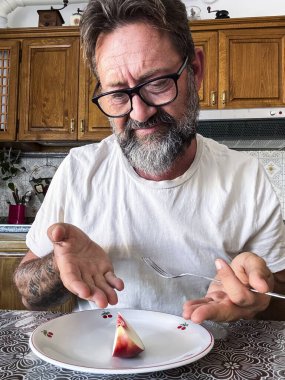 Olgun bir adam, diyet yaparken aşırı beslenme kontrolünde yemek için tabakta küçük bir meyve parçasına bakar. Üzücü ve istifa etmiş bir ifade. Karbonhidrat yok. Düşük kalori kavramı yağ kaybettirir.