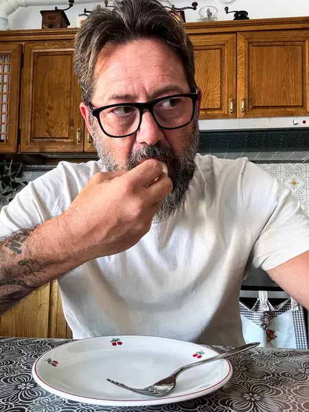 stock image adult man finish eating a healthy diet lunch with fruit and low quantity to reduce fat and gain health. Portrait of mature male eating fruit in the kitchen alone at home in dieting activity indoor