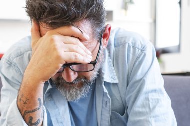  Kanepede tek başına oturan bir adam alnına dokunarak sorunları ve çözümleri düşünüyor. Ekonomik kriz ayrılığı, boşanmak olgun bir erkeğin oturma odasında endişeli ve stresli olması.