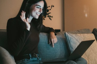 Mutlu esmer kız dizüstü bilgisayarla el sallıyor sanal sohbet videosunun tadını çıkarıyor uzaktan sanal görüşmede, rahatlamış ve arkadaşlarıyla konuşuyor..