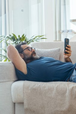 Adam rahatlamak için kanepede uzanmış cep telefonuyla internette geziniyor ya da sosyal medya içeriklerini karıştırıyor. Teknolojisi ve bağlantısı olan tembel insanlar. Akıllı telefon uygulamasının tadını çıkarıyorum.