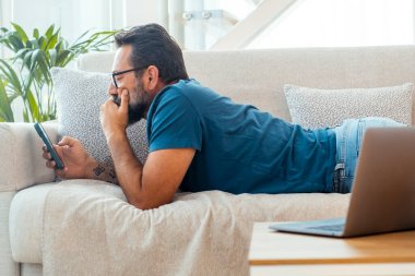 Adam rahatlamak için kanepede uzanmış cep telefonuyla internette geziniyor ya da sosyal medya içeriklerini karıştırıyor. Tembel öğleden sonra, teknolojisi ve bağlantısı olan insanlar. Akıllı telefon uygulamasının tadını çıkarıyorum.