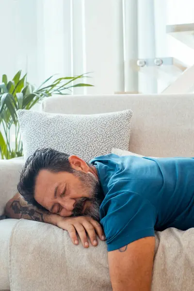 stock image  man fall asleep at home for afternoon nap laying on the sofa with open laptop on the table. Tired people sleep during the daylight. Overwork stress concept lifestyle health. Sleeping on couch