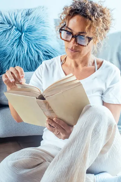 Sakin bir kadın evde rahatlama aktivitesi üzerine kitap okuyor. Sağlıklı olmak ve oturma odasında dinlenmek. Dişi insanlar pazar günleri yerde oturup kitap okuyup eğleniyorlar. Mutlu yaşam tarzı bayan.