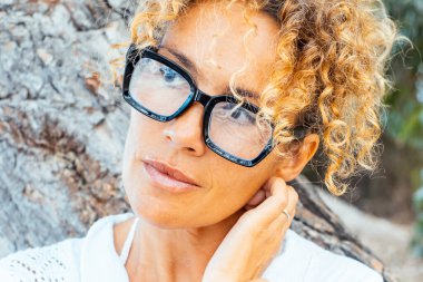 Siyah gözlük takan çekici yetişkin bir kadının tatlı portresi ve açık havada rahat rahat boynuna dokunmak tek başına rahatlama aktivitesi. Bir kadın bakıyor ve düşünüyor. Güzellik bakımı yüzü