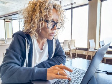 Gemi gezisi sırasında masada oturan güzel sarışın yönetici. Kıvırcık saçlı ve siyah gözlüklü bir kadın seyahat ederken laptop kullanıyor. Dijital göçebeler kavramı.