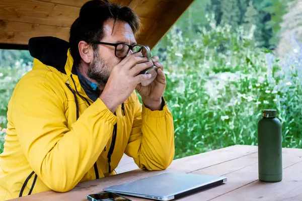 Sakallı gezgin açık havada kahve içiyor. Boş zamanlarında, tahta bir masada oturmuş özgürlüğün ve yolculuğun tadını çıkarıyor. Çevrimiçi olarak her yerde laptop bağlantısı olan modern işçiler. 