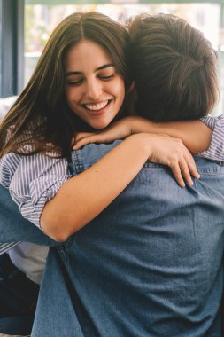 Young couple embracing with joy and excitement while sitting on the sofa at home, celebrating their reunion after a period of separation.  clipart