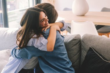 Evdeki kanepede kucaklaşan neşeli genç çift, ayrılık döneminden sonra kalpten bir kavuşmayı kutluyorlar. Kızın yüzü mutluluk ve heyecan saçıyor, yeniden birlikte olmanın saf duygusunu yakalıyor.