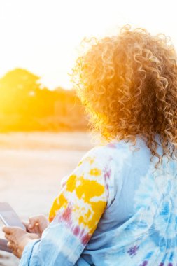 Kıvırcık saçlı kadın arkadan görüldü, güneşin büyülü ışığında yıkandı, doğal manzaraya hayran kaldı. Seyahatin, özgürlüğün ve farkındalığın özünü yakalar. Huzurlu bir ortamda hayatın güzelliğinin tadını çıkarır.