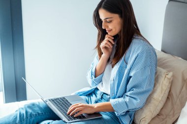 Sıradan bir kot pantolon giymiş düşünceli bir kızın portresi. Evinde dizüstü bilgisayarında web sayfası okurken çenesine dokunuyor. İnternet, gaz veya mobil planlar gibi ev hizmetlerini seçiyor ve gelecekteki planlarını yansıtıyor.