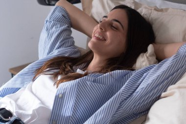 Genç bir kadın evdeki bir yatakta rahat rahat yatıyor, elleri başının arkasında yatıyor, iş gününden sonra gülümsüyor ve huzurlu. Yolculuktan sonra modern milenyum yaşam tarzını, mutluluğu ve bağımsızlığı kucaklamak
