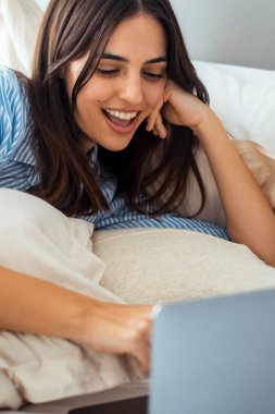 Çekici bir kadın mutlu bir şekilde otel yatağında dizüstü bilgisayarında internette geziniyor, e-postaları ve uyarıları okuyor.. 