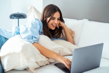 Çekici bir kadın mutlu bir şekilde otel yatağında dizüstü bilgisayarında internette geziniyor, e-postaları ve uyarıları okuyor.. 