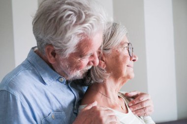 Boş vakitlerinde evde sevgi dolu kucaklaşan olgun bir çiftin yan görüntüsü. Yaşlı bir adam karısını arkadan tutar, onların romantik ve koruyucu bağlarını yakalar, son sınıfların sevgisini gösterir ve uzun süreli aşklarını gösterir.