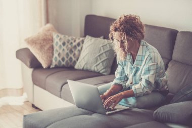 Yetişkin bir kadın rahat evindeki kanepesinde dizüstü bilgisayarla çalışıyor, internette geziniyor, e-posta yazıyor ve günlük işleri yönetiyor. Uzak çalışma ve serbest profesyonellikle modern yaşam tarzını yakalıyor