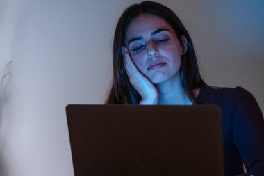 Late-night portrait of a tired and exhausted woman working on her laptop, showing boredom and frustration. Alone at home, she struggles with insomnia while staring at the computer, unable to sleep due to excessive online work clipart