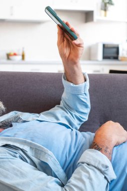 Bir adamın kolunu telefonla kapatın, bir kanepede rahatça uzanırken sosyal medyada dolaşın, çeşitli içeriklere göz gezdirin ve rahatlamak için bildirileri ya da e-postaları okuyun.