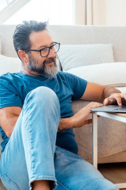Bir adam evinde interneti gezmek için dizüstü bilgisayarını kullanır. İş için ya da boş zamanlarında. Rahatlatıcı bir yerde kablosuz bağlantının olduğu modern ve rahat ortamın tadını çıkarır.