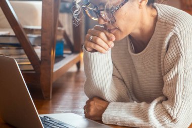 Sıradan ve olgun bir kadın oturma odasının ahşap zemininde yalın ayak yatıyor, internette gezinmek, iş planları üzerinde çalışmak ya da online sohbetler yoluyla arkadaşlarıyla bağlantı kurmak için bilgisayarına odaklanıyor.