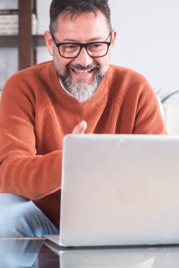 Orta yaşlı bir adam gözlük takıyor ve rahat bir şekilde evdeki bir kanepede oturuyor. Uzaktan kumandalı bir dizüstü bilgisayar üzerinde çalışıyor, serbest işleri kişisel online eğlence aktiviteleriyle birleştiriyor.