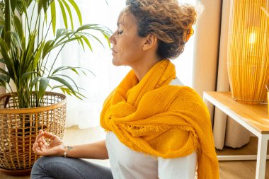 Kadın evde yoga yapıyor ve fiziksel ve zihinsel refah için meditasyon yapıyor. Dengeyi sağlamak için günlük esneme egzersizleri, nefes teknikleri ve gevşeme hareketleri uyguluyor..