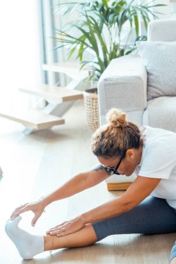 Çeşitli yoga pozları veren ve evinde oturma odasında yerde esneme egzersizleri yapan bir kadın, sağlıklı yaşam tarzının bir parçası olarak esneklik, denge ve daha güçlü bir vücut hedefliyor.