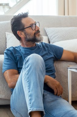 50 yaşında bir adam oturma odasında yerde oturuyor, günlük kıyafetler giyiyor, internette gezinmek için küçük bir masaya dizüstü bilgisayar koyuyor, sosyal medyayla meşgul oluyor ve boş zamanlarında internette çalışıyor.