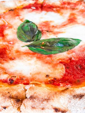 Çıtır çıtır bir hamurlu pizza, taze mozzarella, domates sosu ve mis kokulu fesleğen yaprağı içeren margherita pizzasının ayrıntılı görüntüsü, İtalyan mutfağının simgesel basitliğini ve lezzetlerini gözler önüne seriyor.