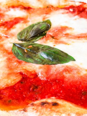 Çıtır çıtır bir hamurlu pizza, taze mozzarella, domates sosu ve mis kokulu fesleğen yaprağı içeren margherita pizzasının ayrıntılı görüntüsü, İtalyan mutfağının simgesel basitliğini ve lezzetlerini gözler önüne seriyor.