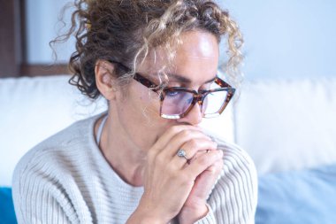 Evinde bir kadın, üzgün bir ifadeyle kanepede oturuyor, hayatını yansıtıyor, kendini soyutlanmış, endişeli ve geleceği hakkında güvensiz hissediyor, menopoz ve tükenmişlikle ilgili duygusal zorluklarla uğraşıyor.