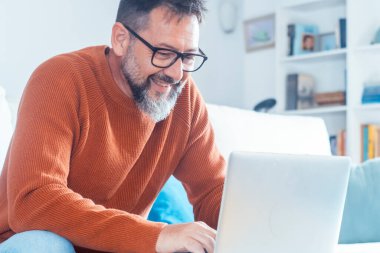 Modern mutfakta dizüstü bilgisayarda çalışan gülümseyen genç adam, e-postaları kontrol eden, sosyal ağda mesaj yazan, internet bankacılığı hizmetini kullanan mutlu genç adam, bilgi arayan