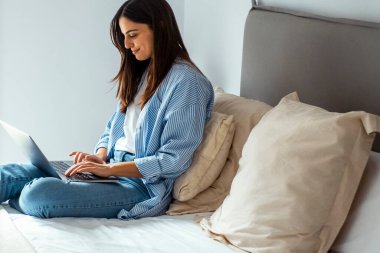 Sabahları rahat giyinen bir kadın otel odasında ya da yatak odasında kablosuz internet bağlantısı olan bir dizüstü bilgisayarla yazı yazıyor. Serbest meslek ve öğrenci yaşam tarzı kavramı, seyahatte