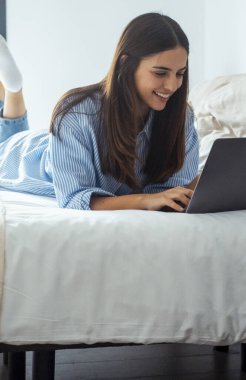 Dijital sabah. Çevrimiçi eğlence. Ev tatili. Hafta sonu istirahati. Rahat kadın film izlemekten zevk alıyor ya da dizüstü bilgisayar kullanarak ışık odasında gülümsüyor. Tembel genç kadın.