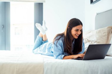 İş seyahati için evde ya da otel odasında dizüstü bilgisayar kullanan sevimli ve neşeli bir genç. İnsanlar ve teknoloji, bilgisayar web sayfasında yazma, şifre yazma veya kişisel ayrıntılar