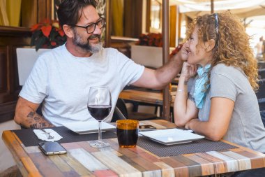 A couple enjoys a joyful and intimate moment during lunch at an outdoor restaurant, laughing together as the man caresses the woman's cheek, sharing a peaceful conversation in a relaxed atmosphere. clipart