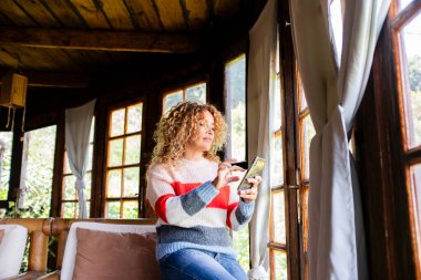İçerde oturan kadın arkadaşlarıyla iletişim kurmak için akıllı telefonunu kullanıyor, internette geziniyor, mesajlar yolluyor, profesyonel ve kişisel görevlerini yönetiyor, ve boş zamanlarının tadını çıkarıyor.