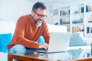 Modern mutfakta dizüstü bilgisayarda çalışan gülümseyen adam, e-postaları kontrol eden, sosyal ağda mesaj yazan, internet bankacılığı hizmetini kullanan mutlu genç erkek, bilgi arayan