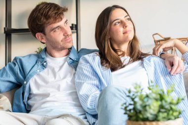 Genç çift rahat bir dairede kanepede oturuyor, yan tarafa bakarken gülümsüyor ve sarılıyor, gelecekteki planlarını, mutlu ilişkiyi, rahat yaşam tarzını, pozitif ruh halini, ev içini düşünüyorlar.