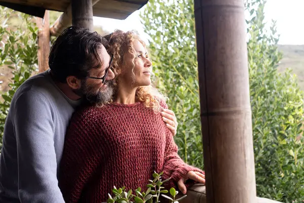 Mutlu bir yetişkin çift balkonda birlikte sakin bir anın tadını çıkarır, doğayla iç içe, birlikte parlak bir gelecek düşlerken birbirlerini kucaklarlar, kiralık dairelerinde huzurlu bir tatil yaşarlar.